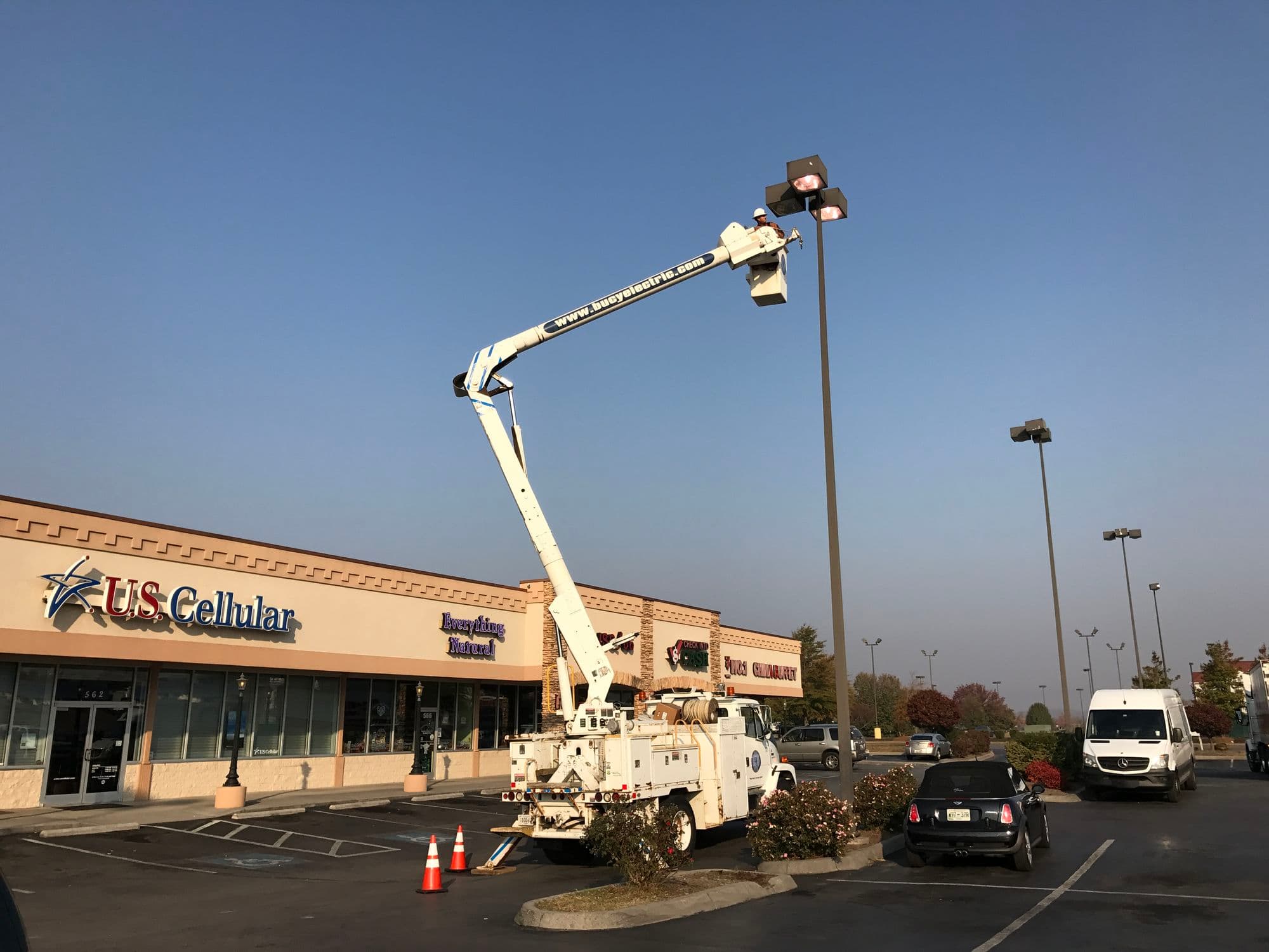 Bucy Electric bucket truck raised to a parking lot light fixture beside a commercial storefront